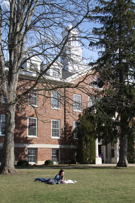 An Albion College student reads on the campus quadrangle. Robinson Hall is in the background.