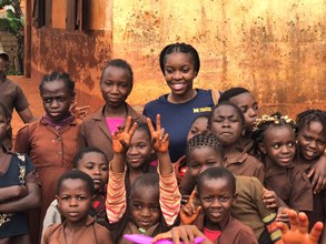 A student posing with children, one of the children is giving two peace signs. 