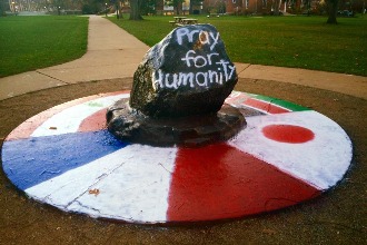 Albion's rock painted black reads 'Pray for Humanity' in white. International flags have been painted on it's base. 