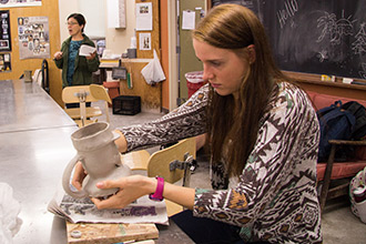 Emily Allison, '18, works with her Toby Jug in her "Ceramics in the Industrial Revolution" Honors class. Professor Lynne Chytilo speaks to the class in the background.